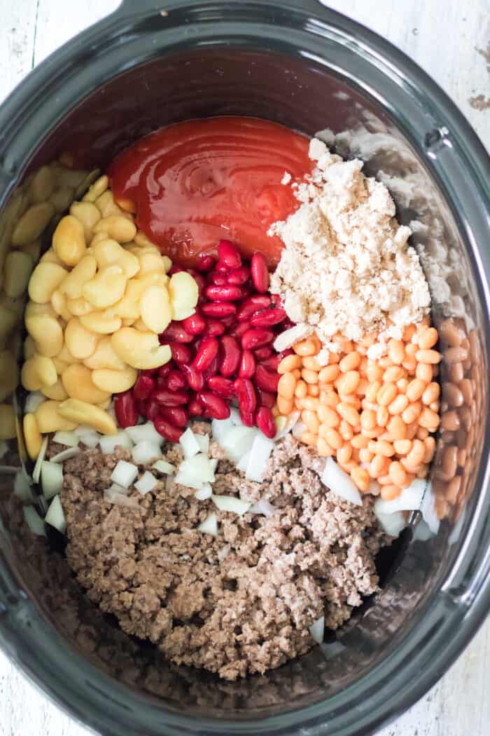 All of the ingredients for slow cooker beans are placed in divided sections in the Crockpot.