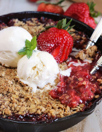 Strawberry Rhubarb Crisp in a black skillet with two scoops of vanilla ice cream on top