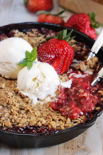 Strawberry Rhubarb Crisp in a black skillet with two scoops of vanilla ice cream on top