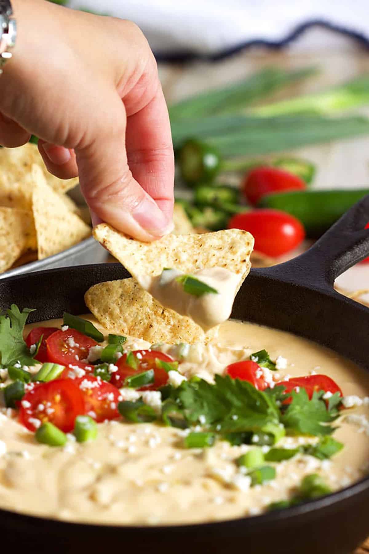 White Queso Dip, Queso Blanco, in a skillet with a hand dipping a chip into it
