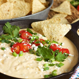 White Queso Dip in a skillet with cilantro and tomatoes on top and chips dipped into it.