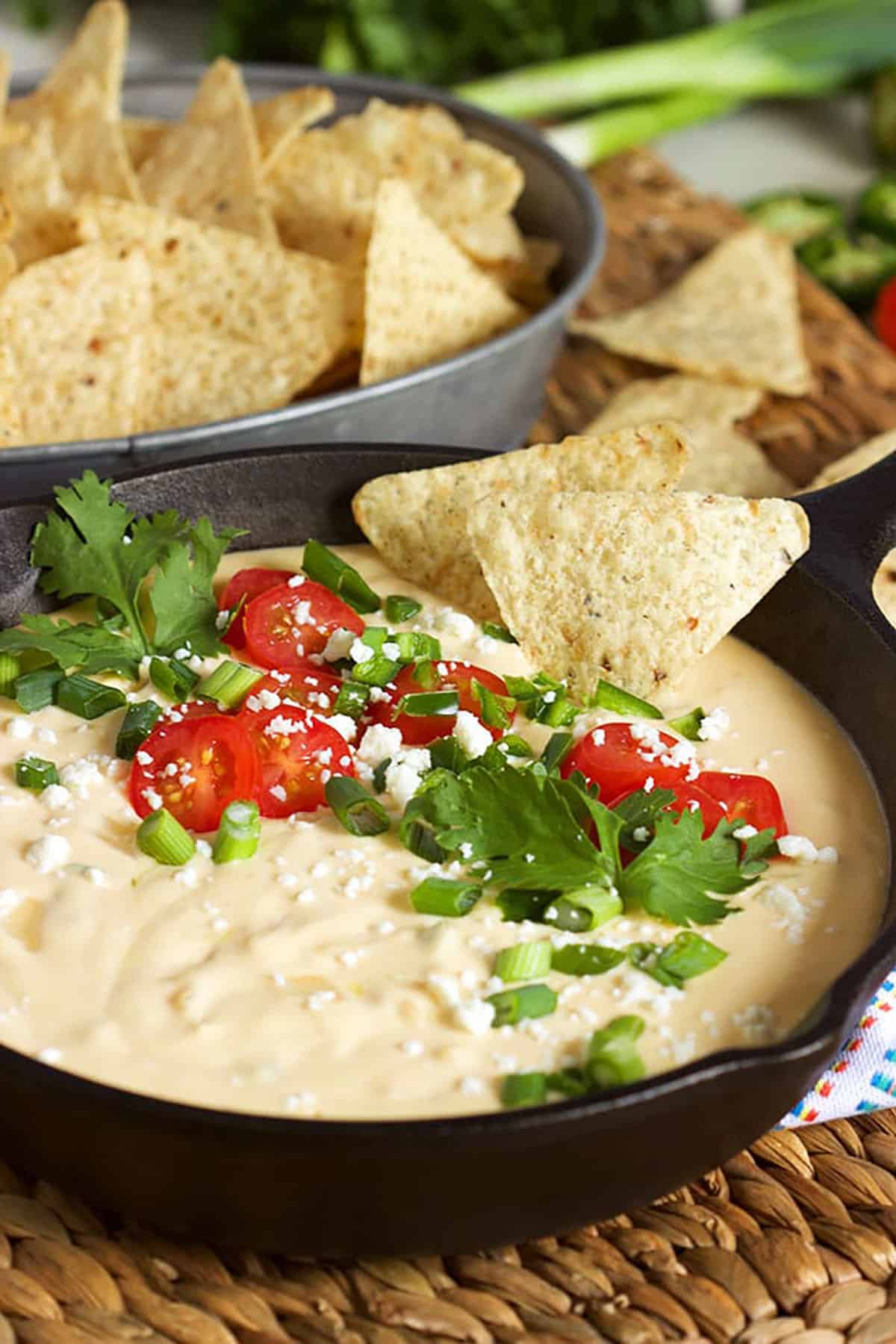 White Queso Dip in a skillet with cilantro and tomatoes on top and chips dipped into it.
