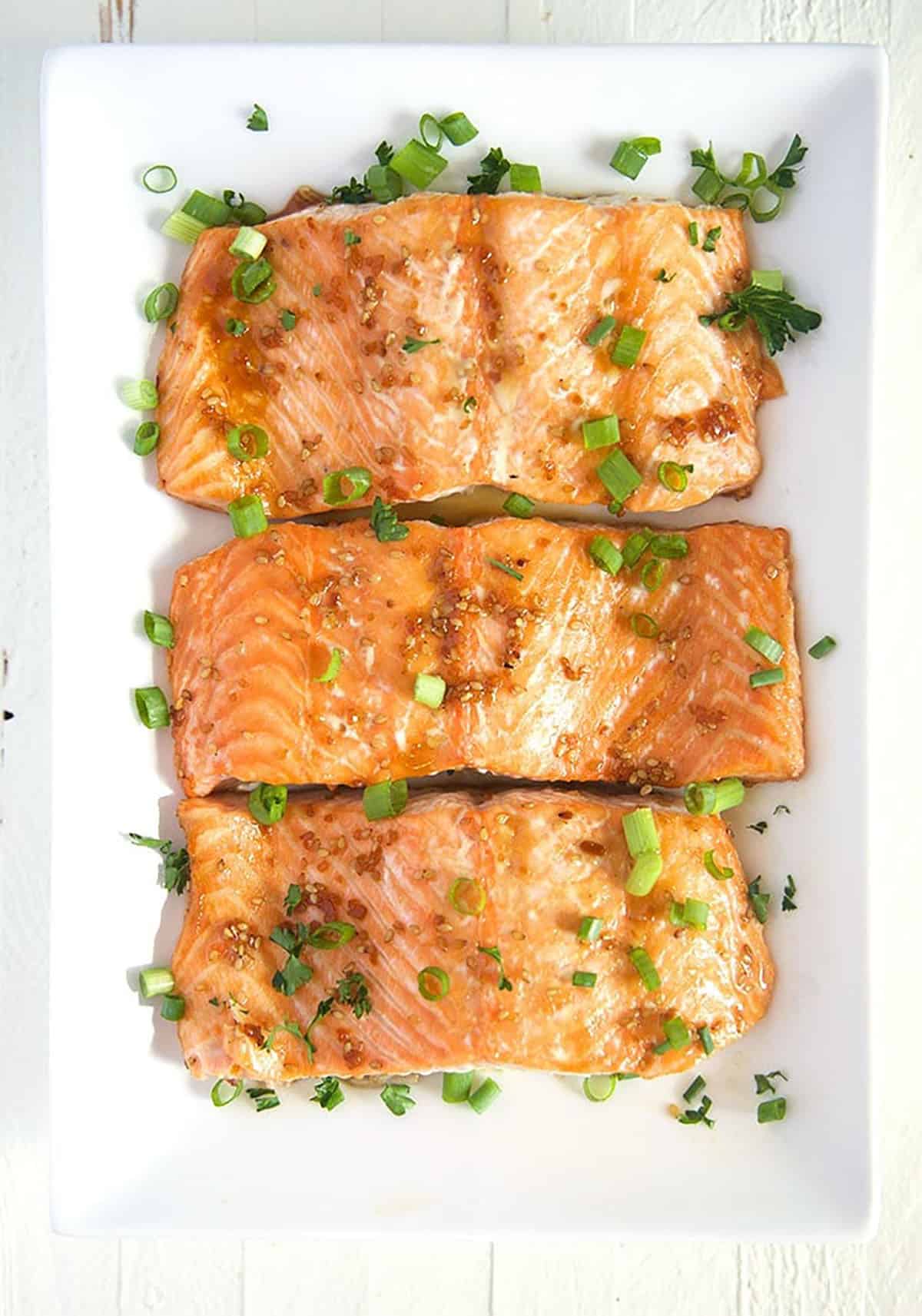 Overhead shot of baked teriyaki salmon on a white rectangle platter.