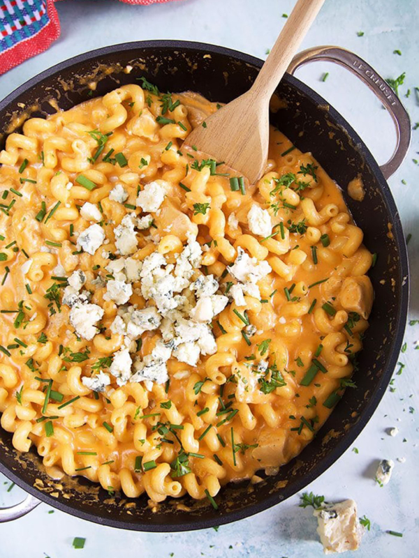Overhead shot of buffalo chicken pasta in a black skillet with a wooden spoon.