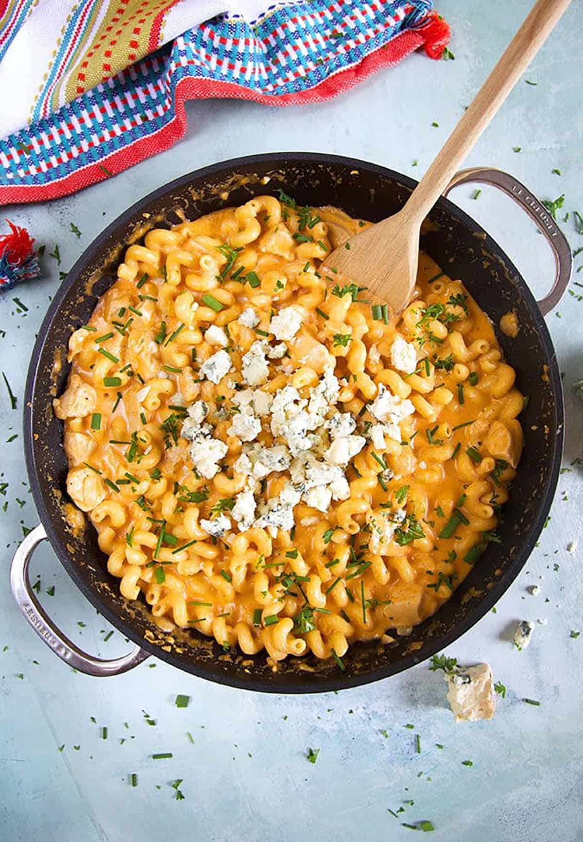 Buffalo Chicken pasta in a black skillet on a blue background.