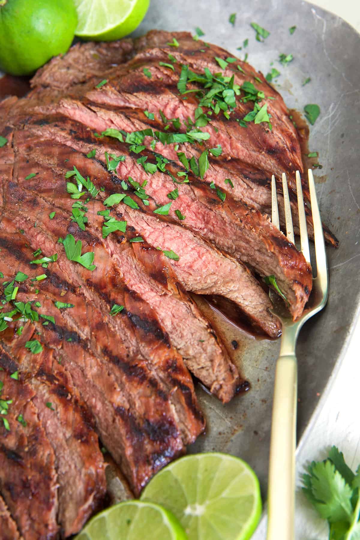 A fork is lifting a slice of carne asada from the serving plate.