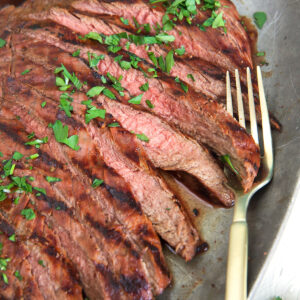A fork is placed on a serving tray full of sliced carne asada.