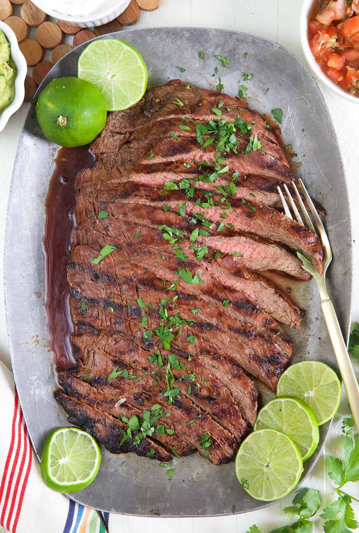 Carne asada has been sliced and is served on a gray serving platter with cilantro and limes.
