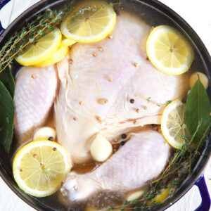 An uncooked whole chicken is submerged in a pot filled with chicken brine.