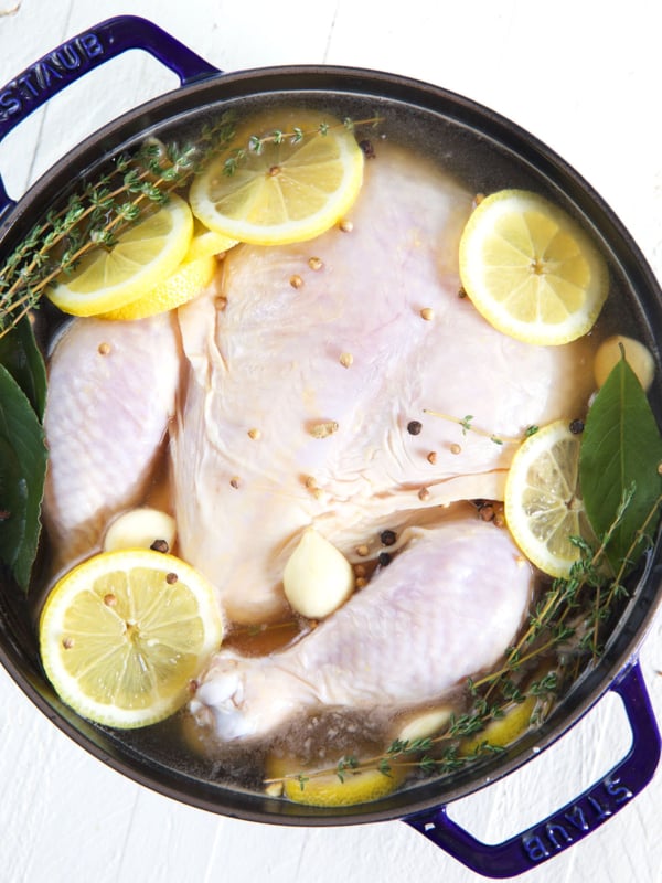 An uncooked whole chicken is submerged in a pot filled with chicken brine.