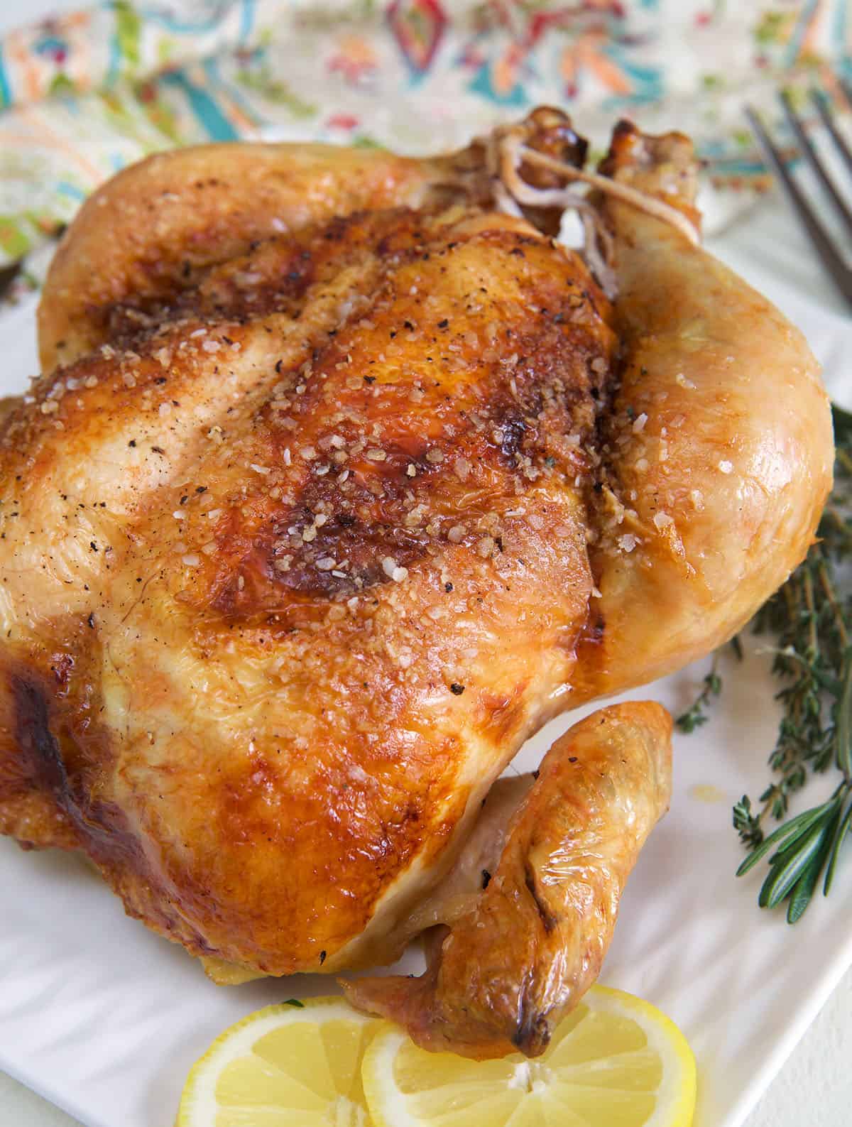 A whole cooked chicken is presented with fresh lemon slices and herbs.