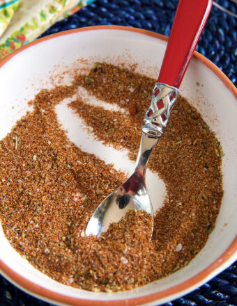 A spoon is mixing together some chili seasoning in a white bowl.