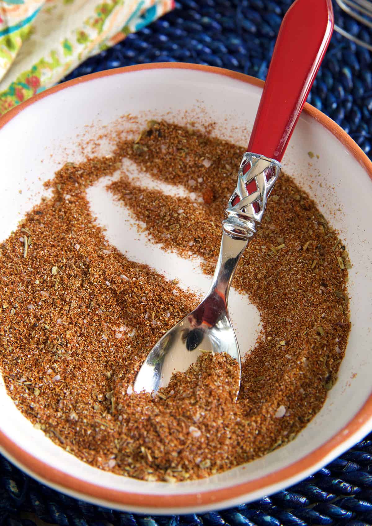 A spoon is mixing together some chili seasoning in a white bowl.