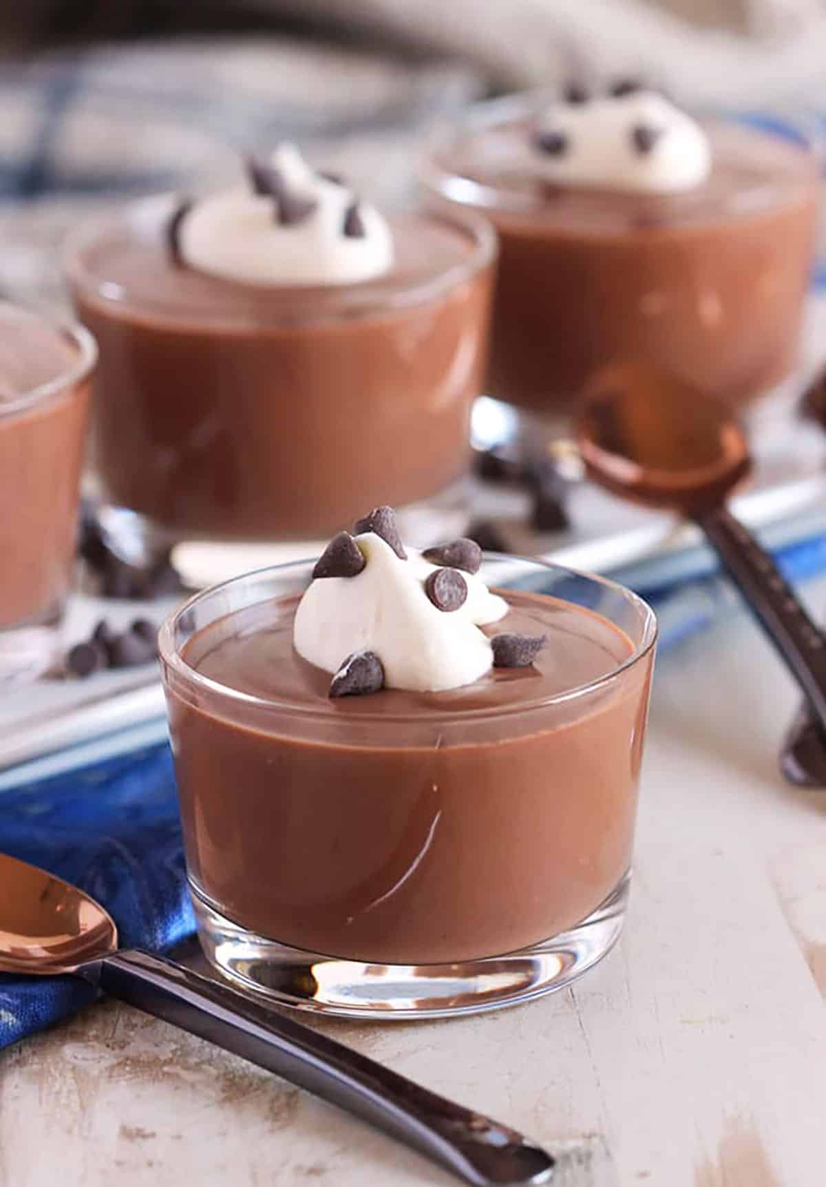 Chocolate pudding in a glass dish with whipped cream and chocolate chips with more dishes on a white platter in the background.