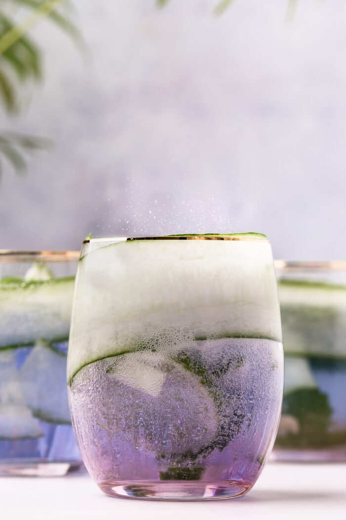 A glass is filled with clear, fizzy liquid and thin cucumber slices.