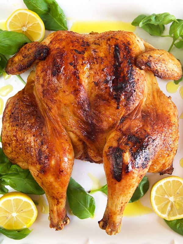 Overhead shot of spatchcock chicken on a white platter with lemons.