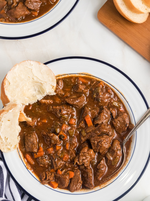 A slice of buttered bread is placed on a bowl full of stew.