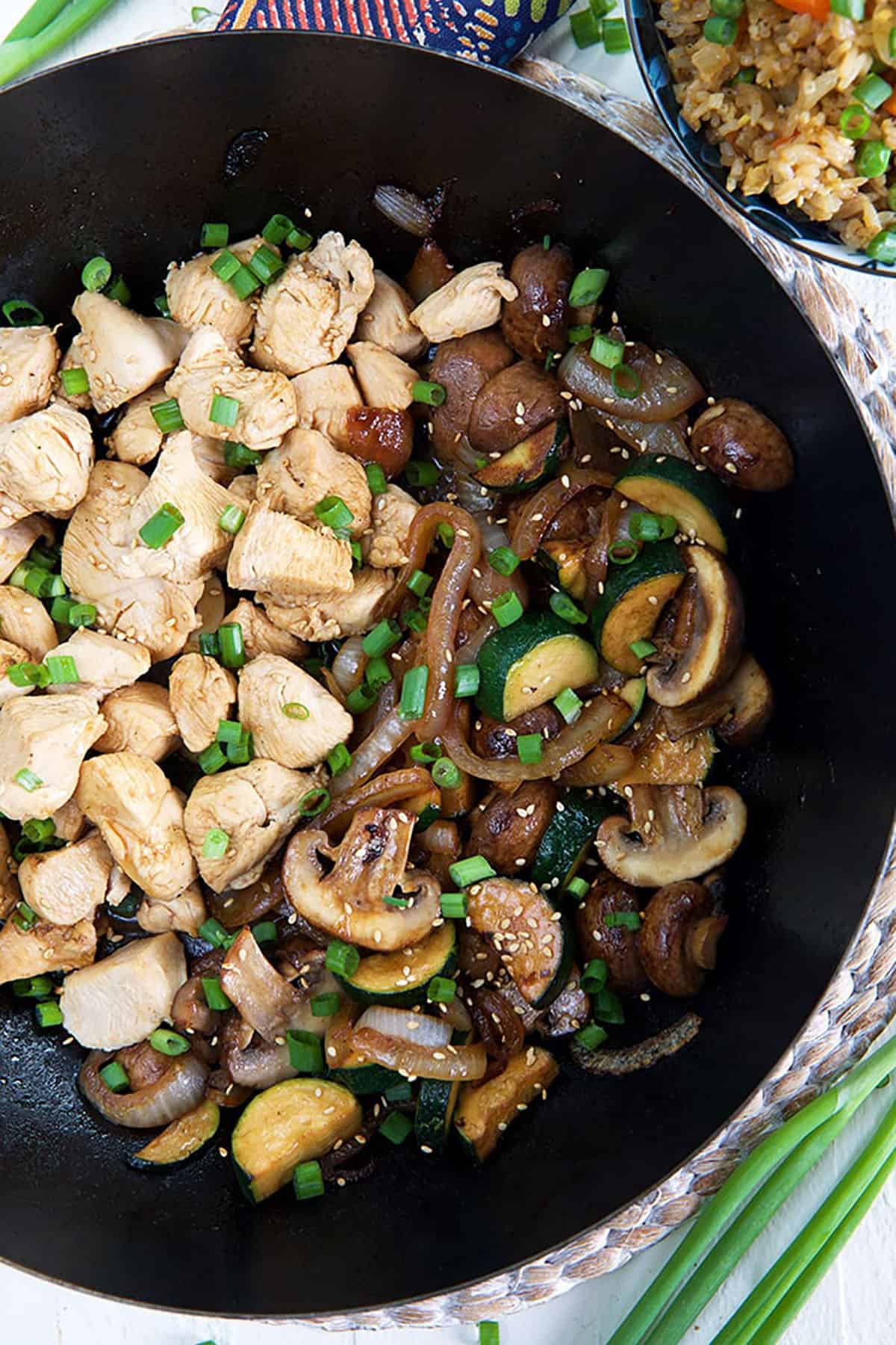 Chicken and veggies are in a large skillet, garnished with chopped green onions.
