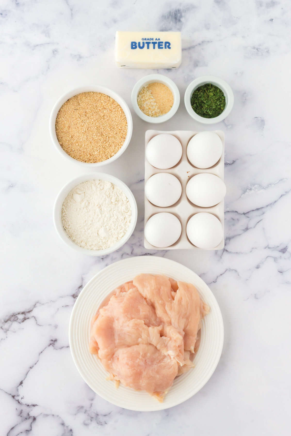 The ingredients for chicken kiev are placed on a white marble countertop. 