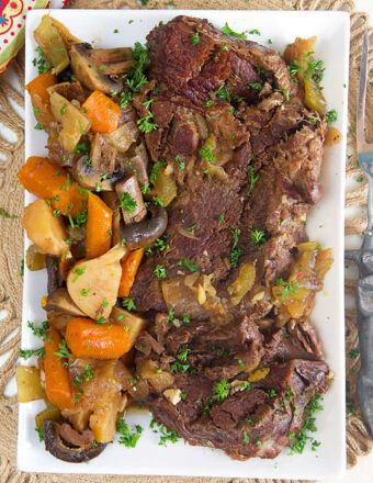 overhead shot of pot roast on a white platter with potatoes, carrots and mushrooms.