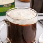 A glass mug filled with irish coffee and whipped cream is placed next to a spoon.