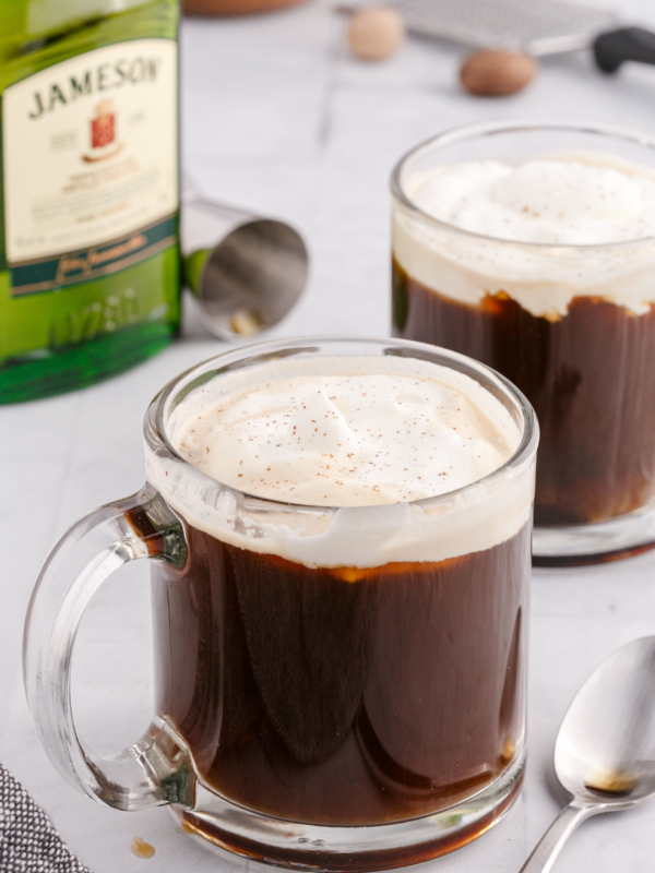 A glass mug filled with coffee and cream is placed in front of a jar of whiskey.