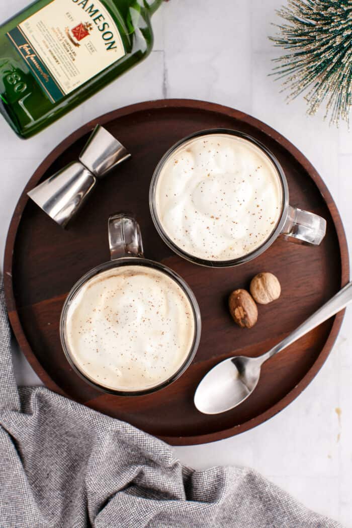Two mugs are filled with Irish coffee and cream on a round serving tray.