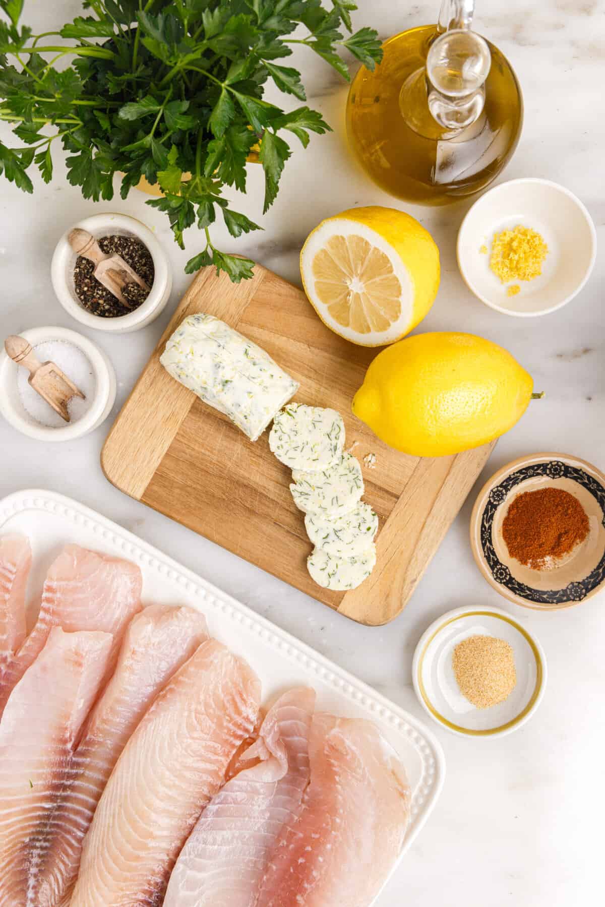 The ingredients for lemon butter tilapia are presented on a white marble surface.