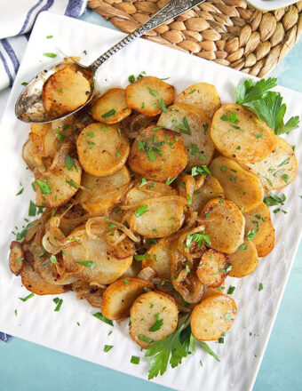 lyonnaise potatoes on a white square platter with a patina'd spoon.