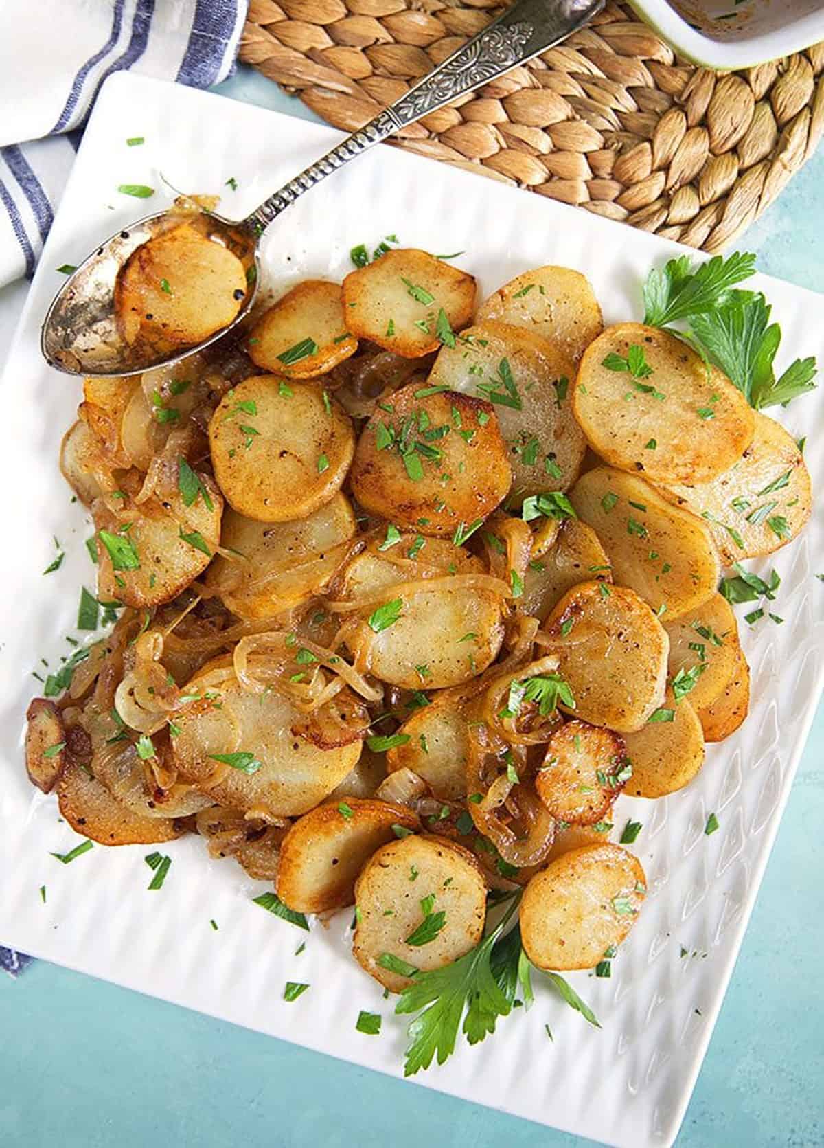 lyonnaise potatoes on a white square platter with a patina'd spoon.