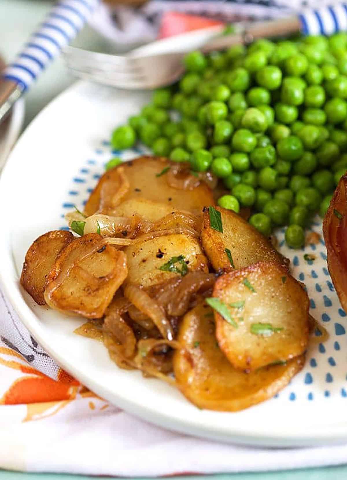 Lyonnaise potatoes on a white plate with peas and meatloaf. 