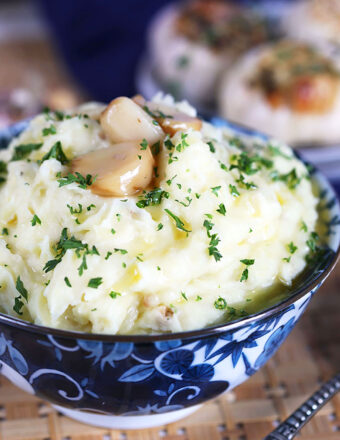 Roasted Garlic Mashed Potatoes with blue and white bowl with roasted garlic cloves on top.