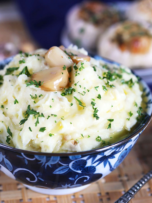 Roasted Garlic Mashed Potatoes with blue and white bowl with roasted garlic cloves on top.