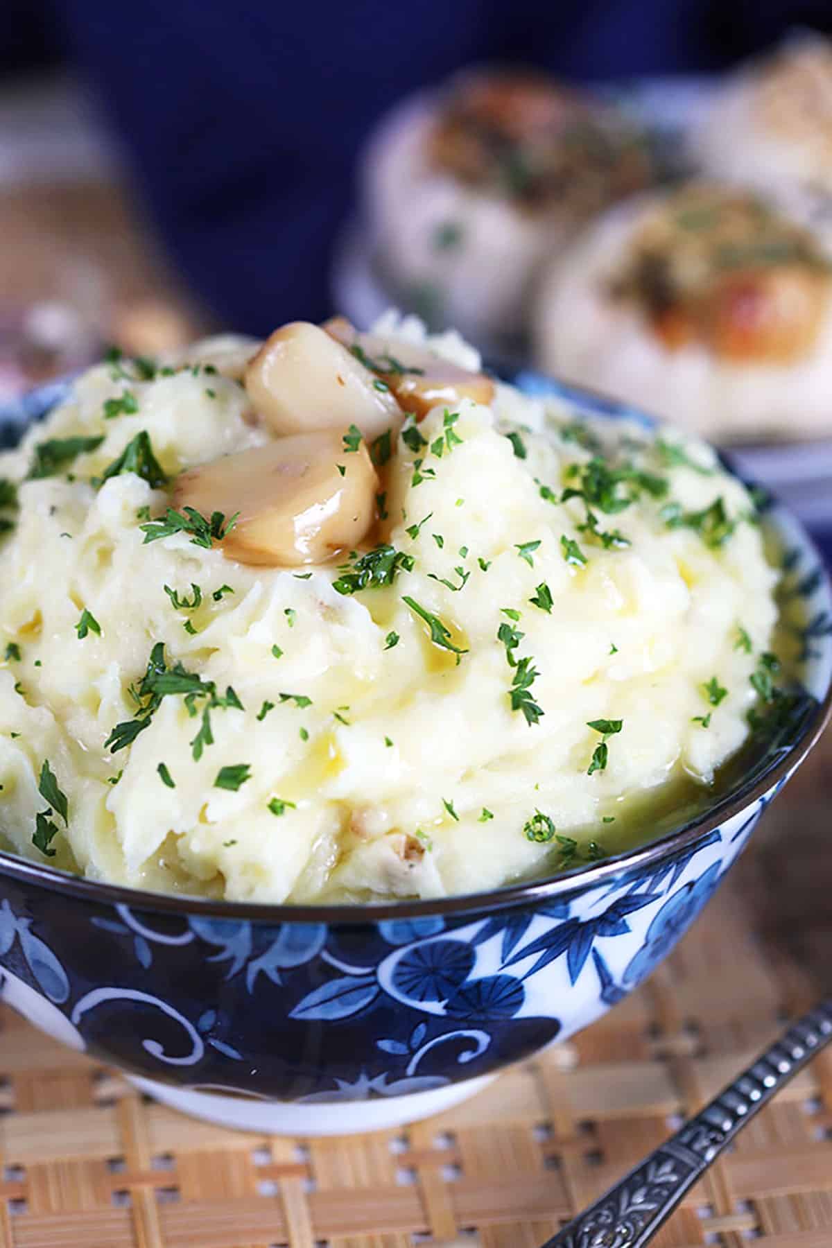 Roasted Garlic Mashed Potatoes with blue and white bowl with roasted garlic cloves on top. 