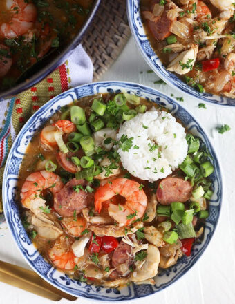 seafood gumbo with a pile of rice and green onions in a blue and white bowl on a white background.