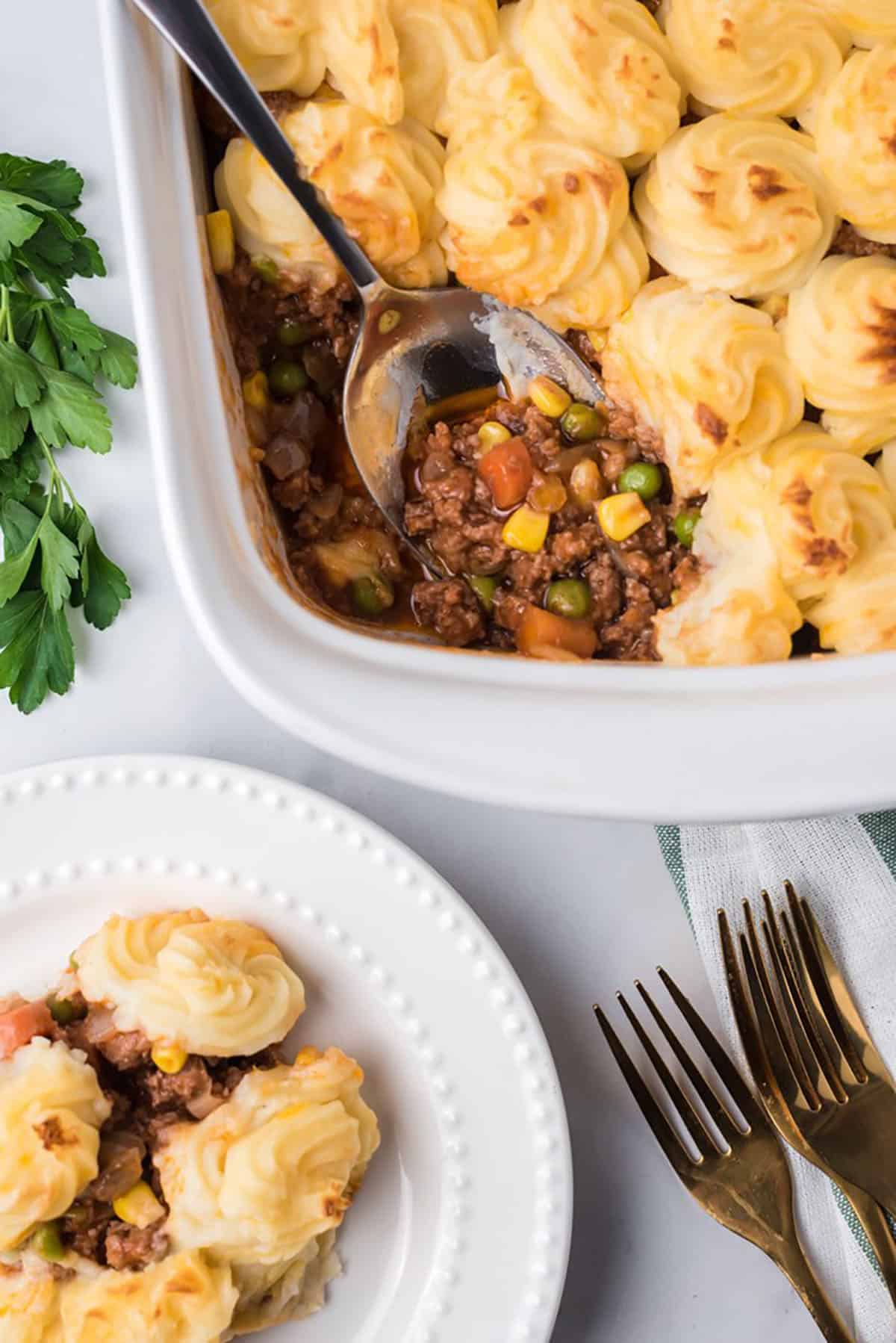 Overhead shot of shepherd's pie in a white casserole dish with a serving spoon.