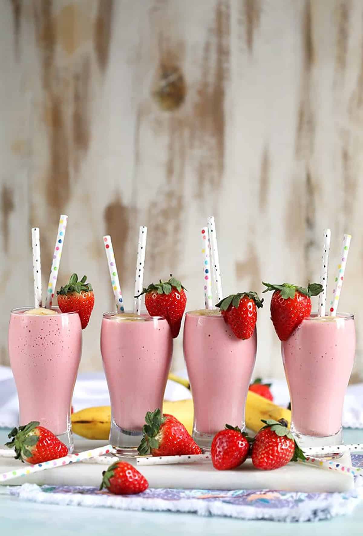 Four Strawberry Banana Smoothies arranged on a marble board with fresh strawberries.