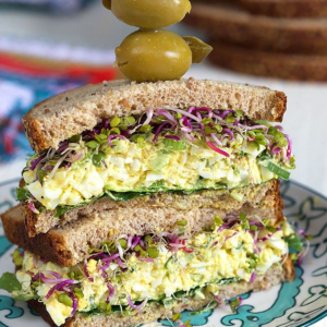 Egg Salad Sandwich halves stacked on top of each other with a toothpick on top with olives on it