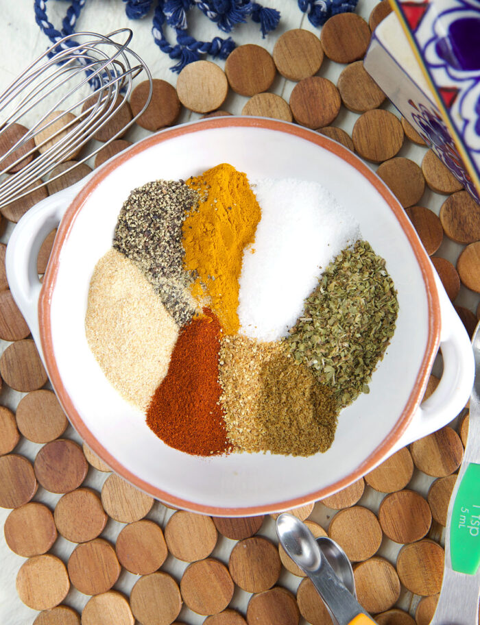 A white bowl is filled with various spices that have not yet been mixed together.