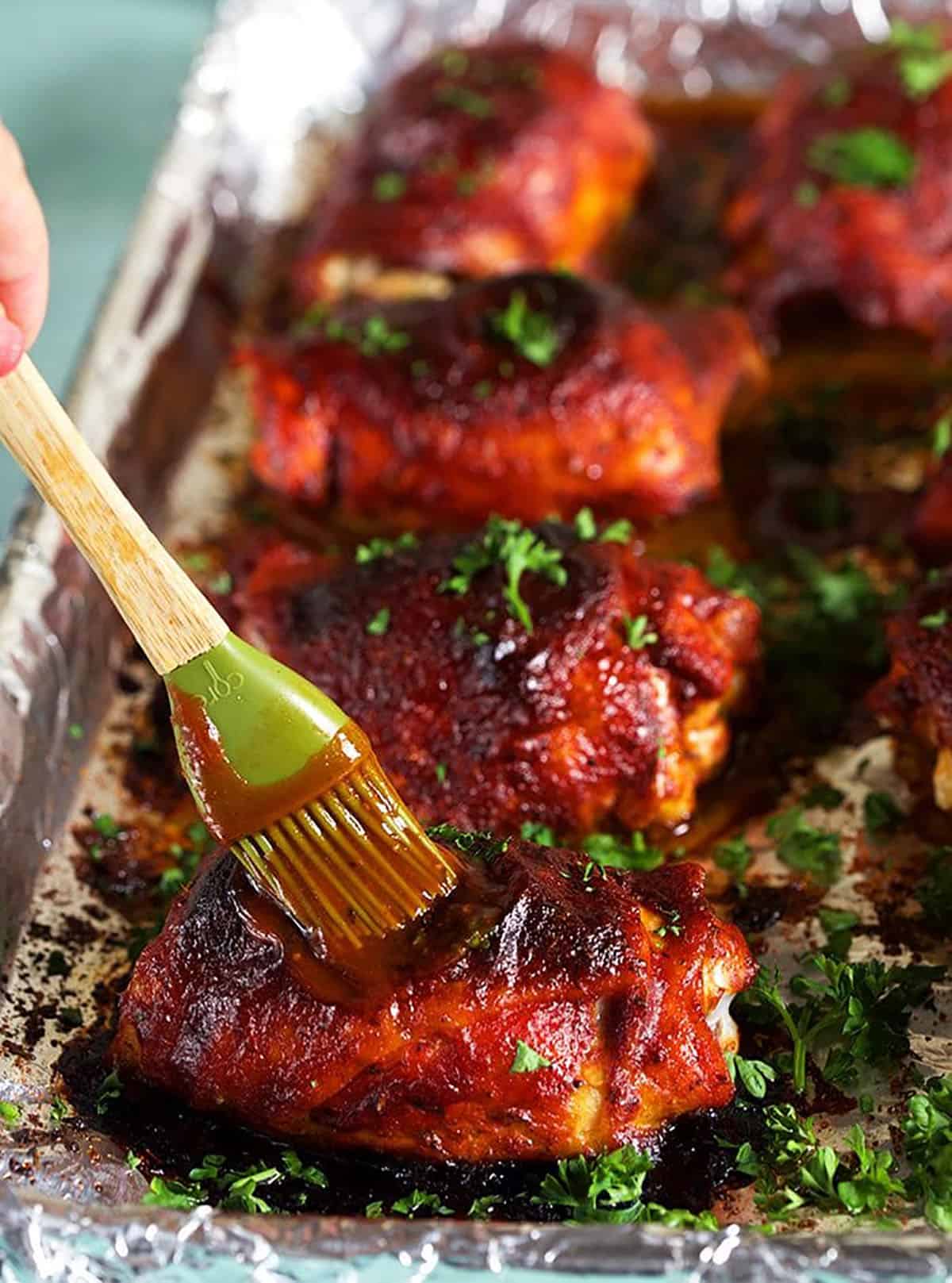 BBQ Chicken on a baking sheet with barbecue sauce being brushed on a thigh.