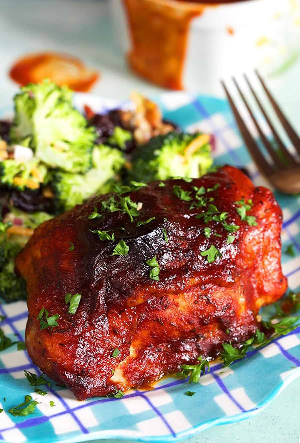 BBQ Chicken thigh on a plaid plate with broccoli salad.