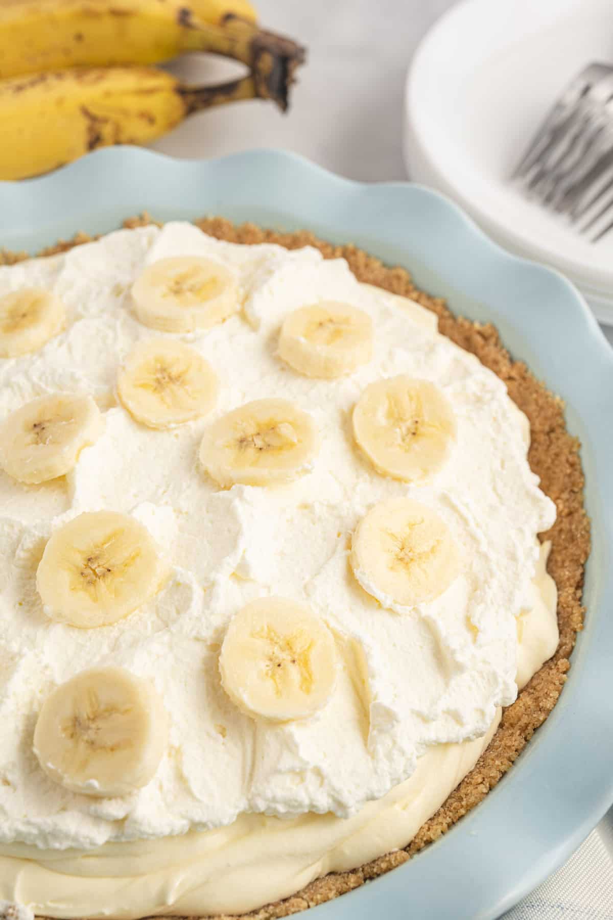 A banana cream pie is placed on a white countertop next to a couple of ripe bananas.