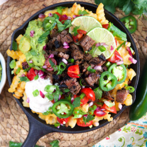A black skillet is filled past the brim with carne asada fries.