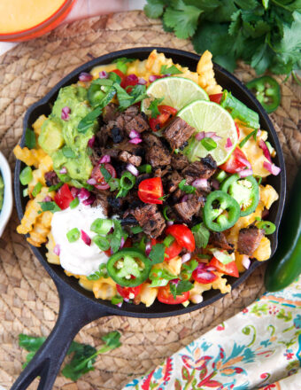 A black skillet is filled past the brim with carne asada fries.