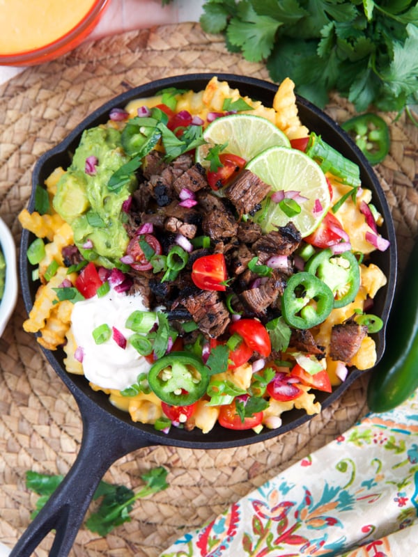 A black skillet is filled past the brim with carne asada fries.