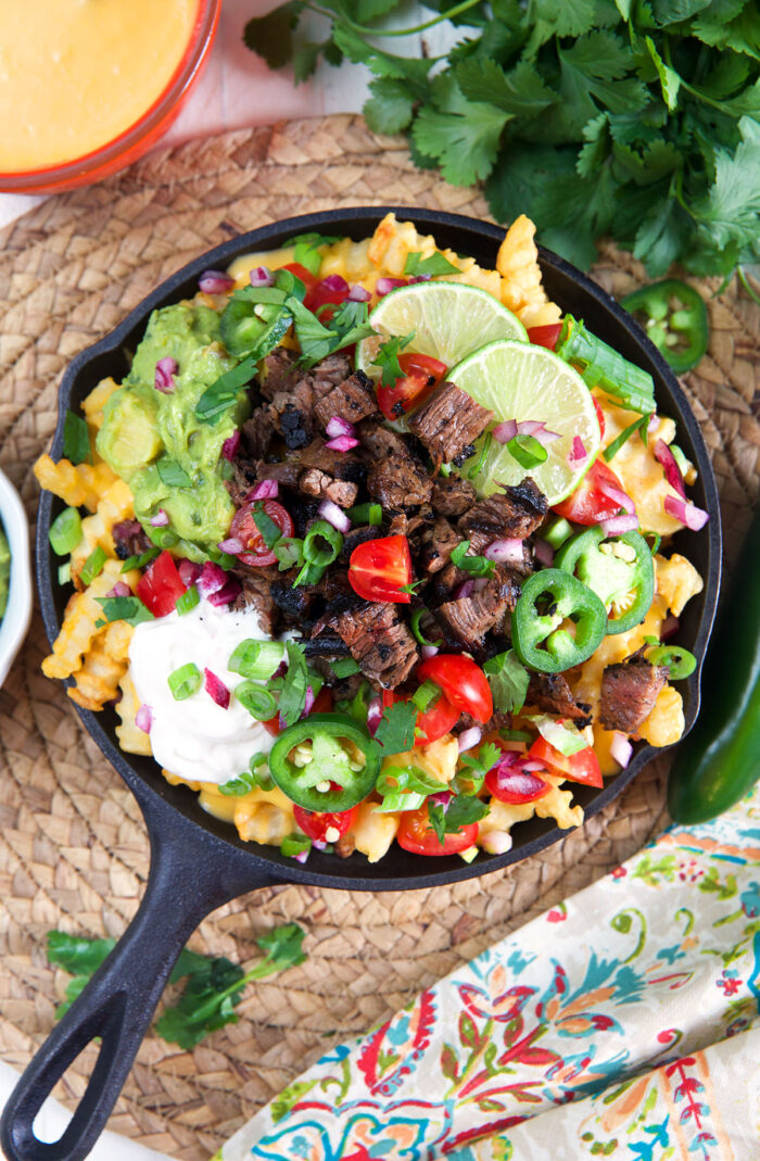A black skillet is filled past the brim with carne asada fries. 
