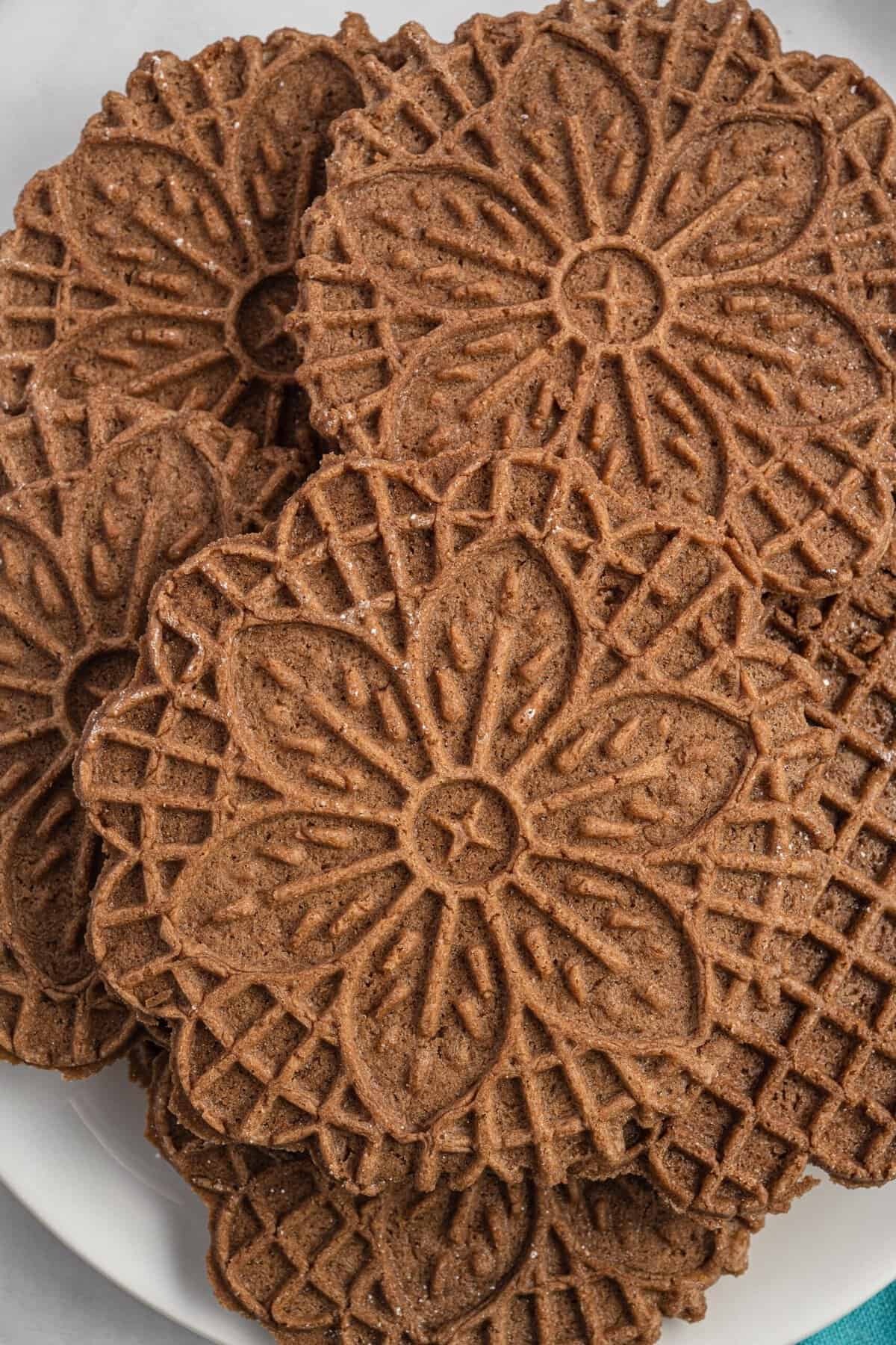 A white plate is stacked with chocolate pizzelle cookies.