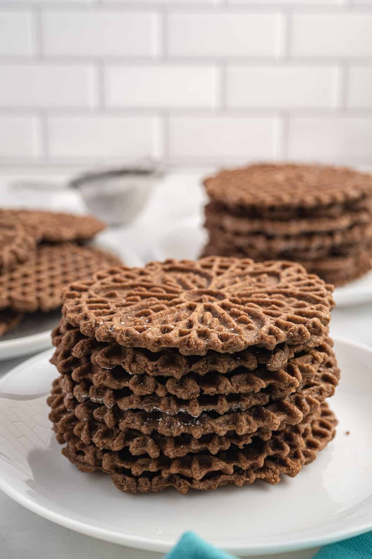 Several stacks of chocolate pizzelles are placed on white plates.