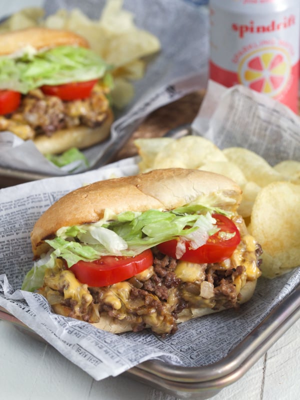 A sandwich is placed on a metal tray next to some chips.