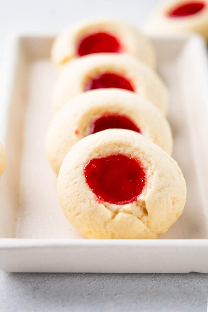 A line of thumbprint cookies is presented on a baking sheet.